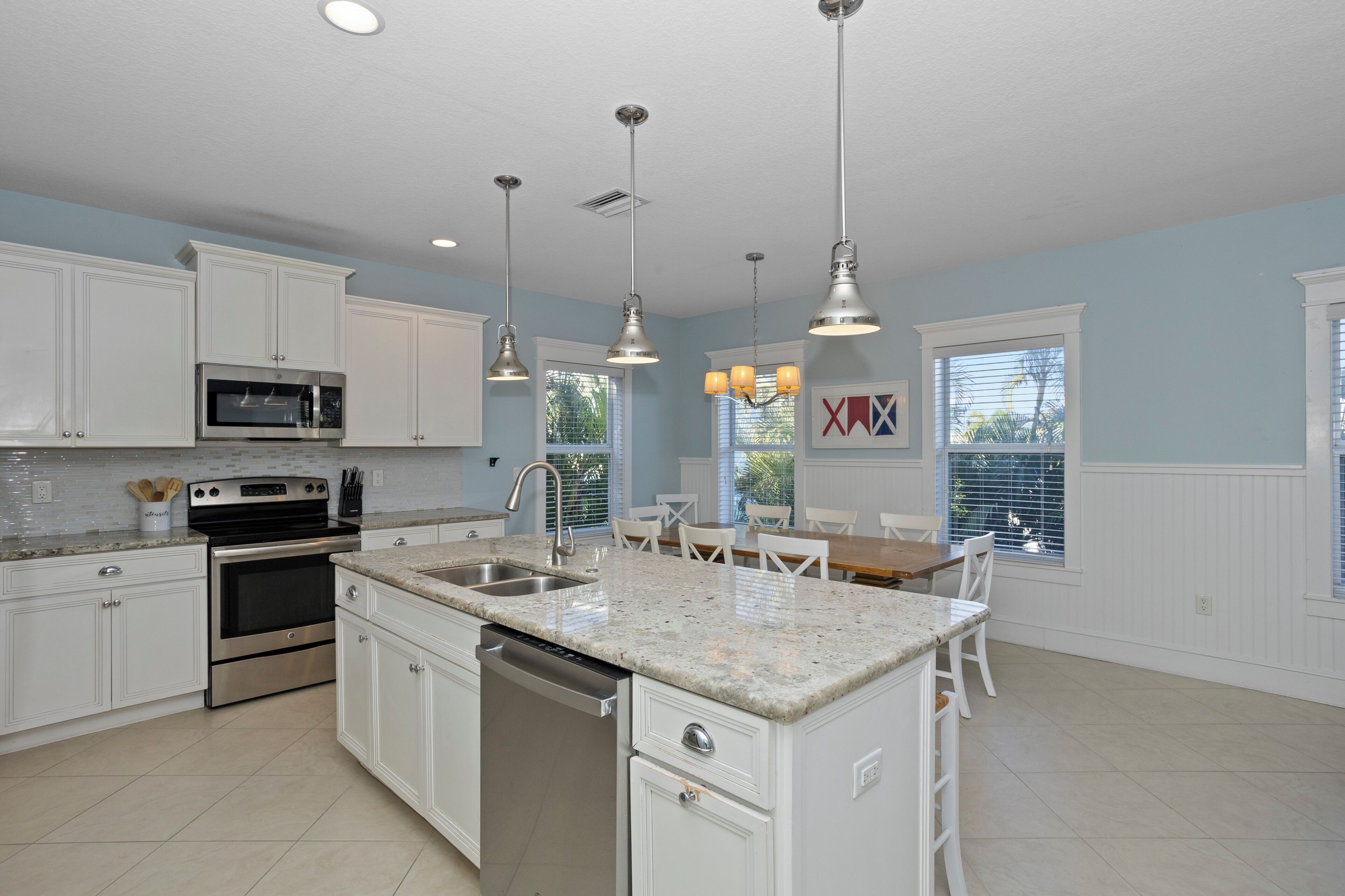 A modern kitchen with white cabinets, stainless steel appliances, granite countertops, pendant lighting, and a dining area with a table and chairs.