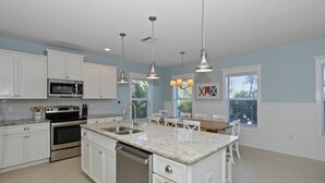 A modern kitchen with white cabinets, stainless steel appliances, granite countertops, pendant lighting, and a dining area with a table and chairs.
