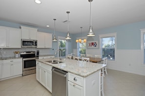 A modern kitchen with white cabinets, stainless steel appliances, granite countertops, pendant lighting, and a dining area with a table and chairs.