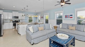 A modern kitchen with white cabinets, a dining area with a blue table, and a gray sofa.