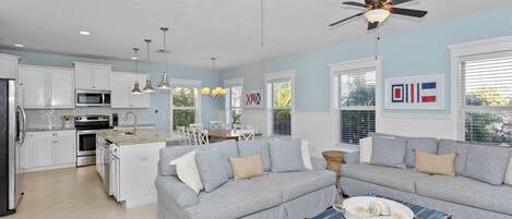A modern kitchen with white cabinets, a dining area with a blue table, and a gray sofa.