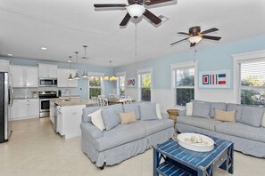 A modern kitchen with white cabinets, a dining area with a blue table, and a gray sofa.