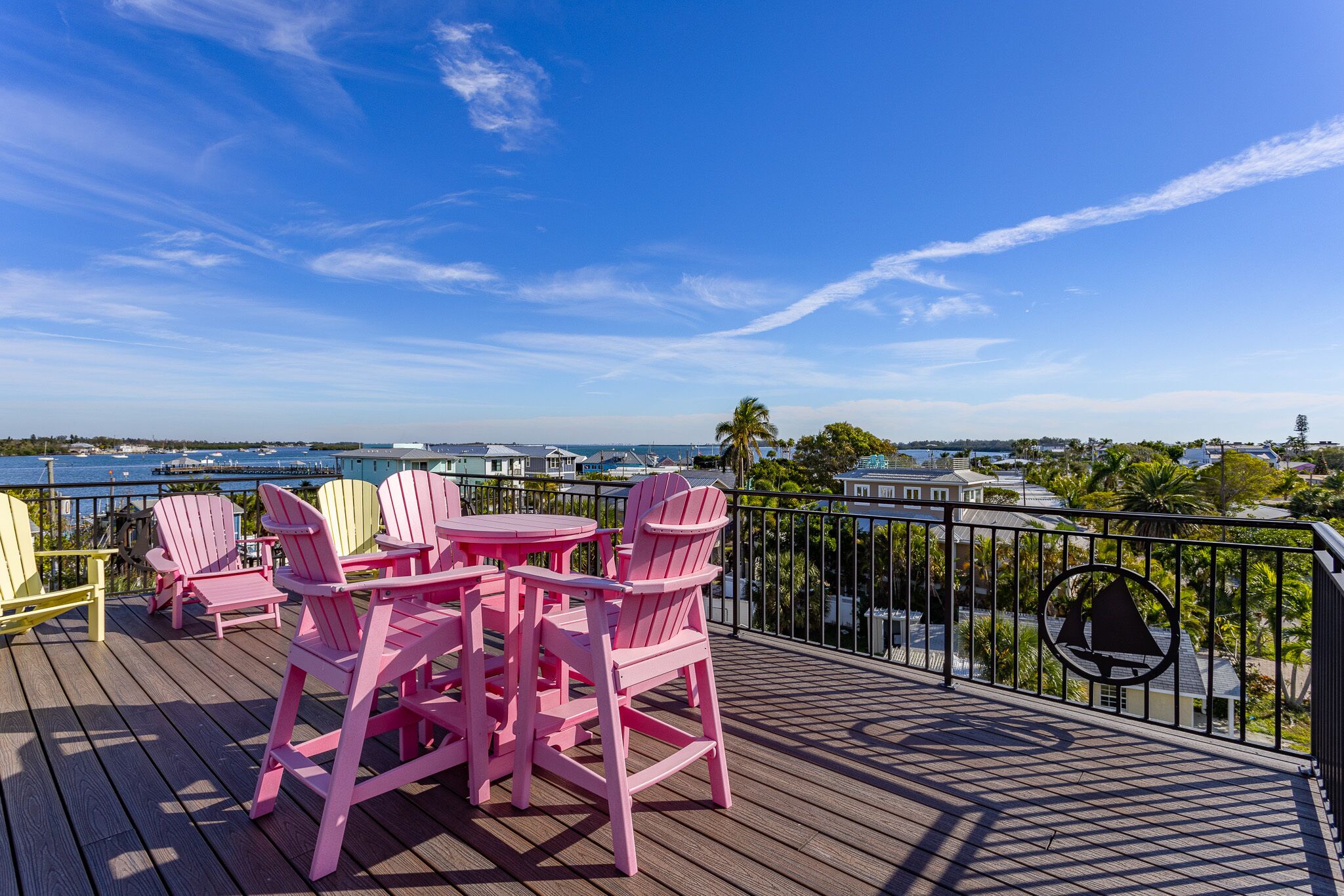 Una terraza con sillas Adirondack rosadas y una mesa, con vistas a un puerto deportivo y edificios.