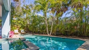 A swimming pool surrounded by palm trees and a building with a white exterior.