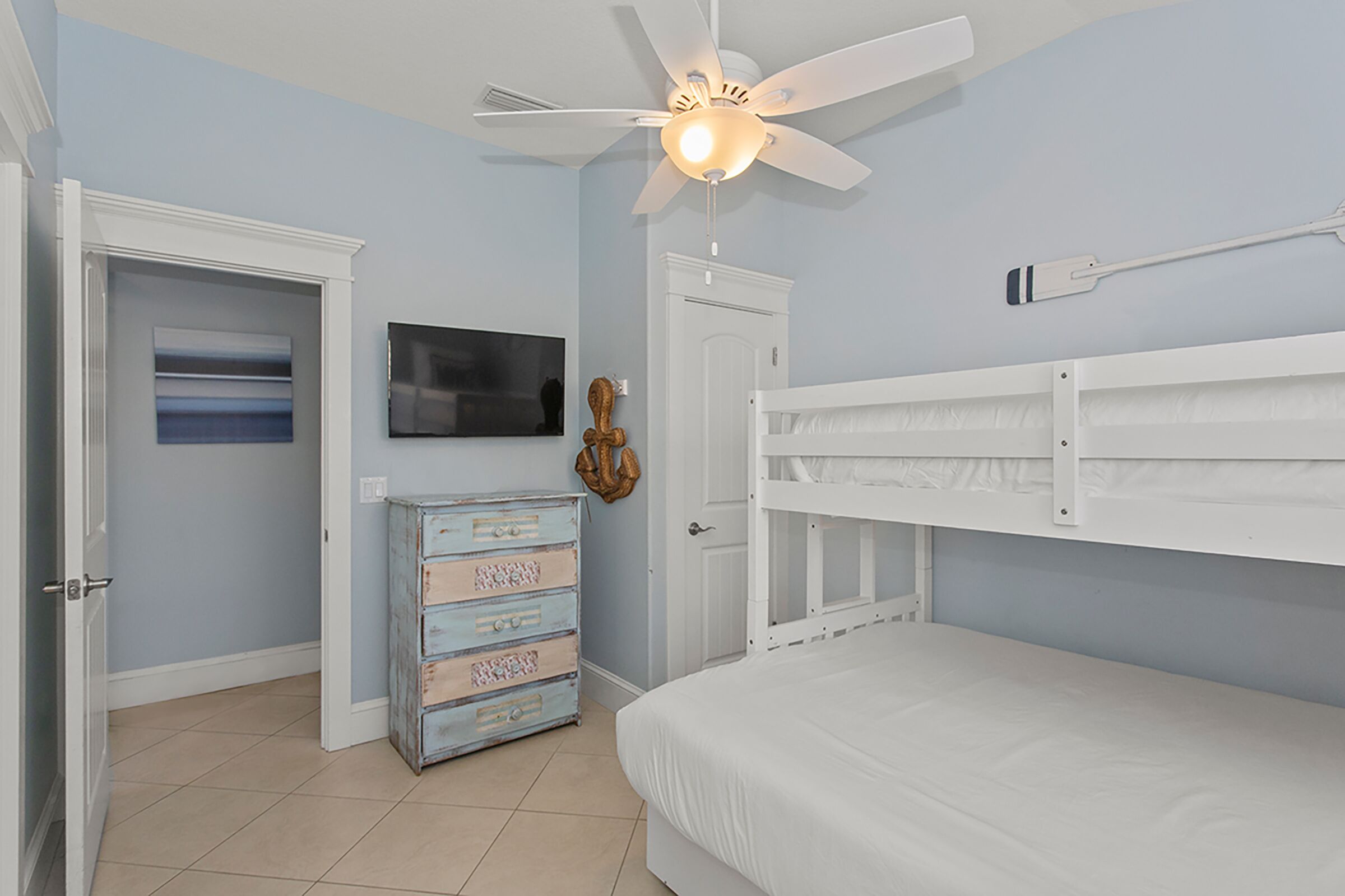 A bedroom with a bed, a ceiling fan, a dresser, a television, and a door.