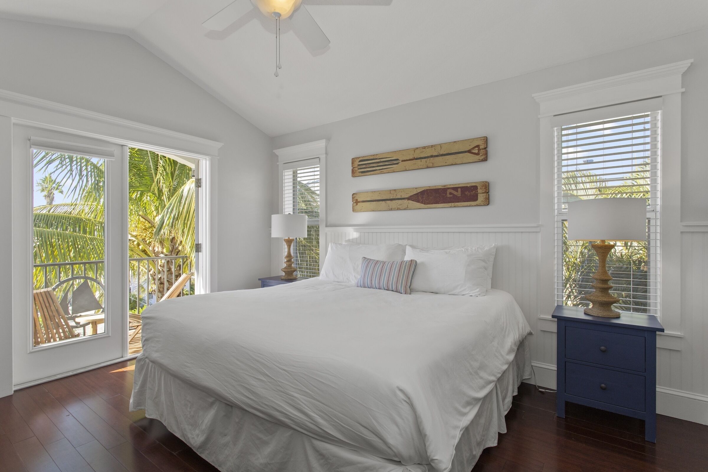 A bedroom with a large bed, a ceiling fan, and a view of the outdoors through a sliding door.