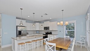 A modern kitchen with white cabinetry, a wooden island with bar stools, pendant lighting, and a view of the outdoors.