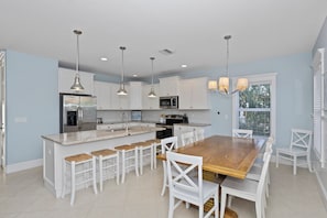 A modern kitchen with white cabinetry, a wooden island with bar stools, pendant lighting, and a view of the outdoors.