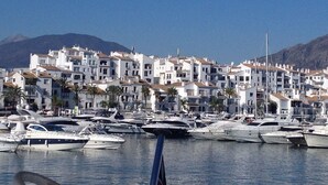 A marina with numerous yachts docked, surrounded by white buildings with red-tiled roofs, and mountains in the background. - Banus Elegant Modern Estudio Next to the Beach (Marbella)