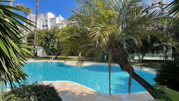 A swimming pool surrounded by palm trees and a white building in the background. - Banus Elegant Modern Estudio Next to the Beach (Marbella)
