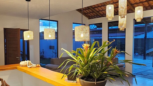 Un intérieur moderne avec un comptoir d’accueil en bois, des plantes en pot et des luminaires suspendus.