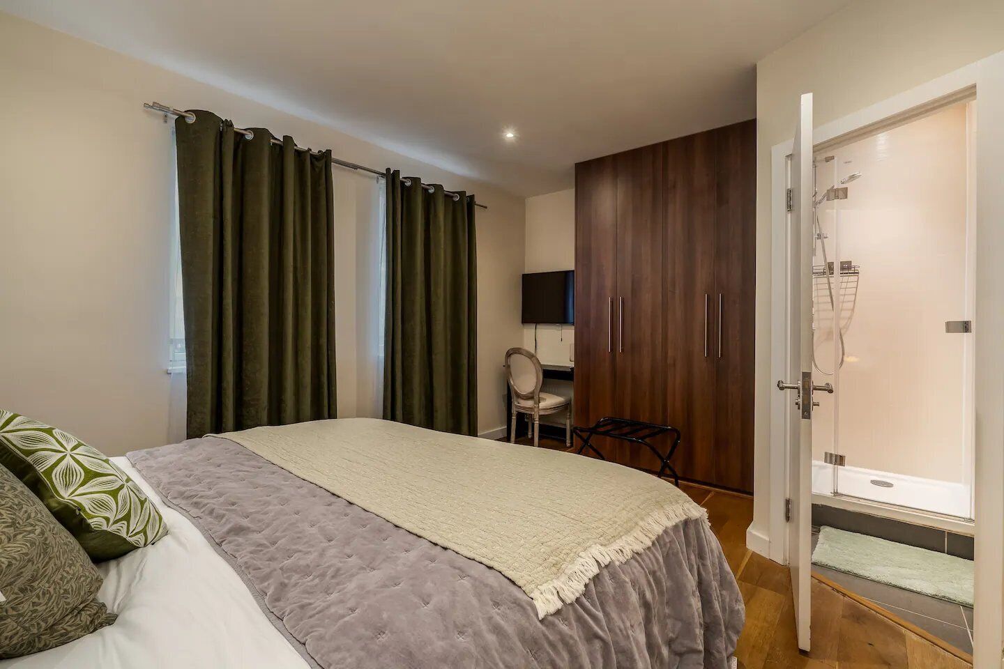 Ein Schlafzimmer mit einem Bett, Vorhängen, einem Sessel, einem Fernseher und einem Kleiderschrank.