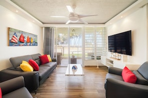 A modern living room with a black leather sofa, a coffee table, and a ceiling fan. - Across from Beach, ocean view, pool, parking, cold AC  (Luquillo)