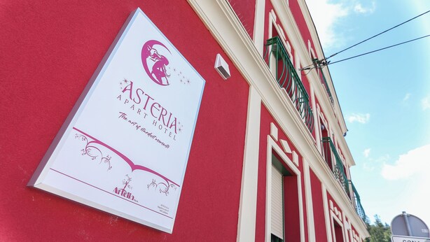 Een hotelschild met een logo en naam, bevestigd aan een rood gebouw met witte details en groene raamkozijnen.