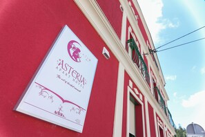 Letrero de hotel con logotipo y nombre, en un edificio rojo con detalles blancos y marcos de ventanas verdes.
