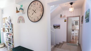 Een gang met een grote wandklok, een groene bank en een trap die naar een andere kamer leidt.