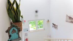 Een kamer met een kleine potplant, een decoratieve woninginrichting, een raam met uitzicht op groen en een witte balustrade.