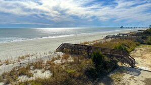 A beach with a wooden boardwalk leading to a pier.