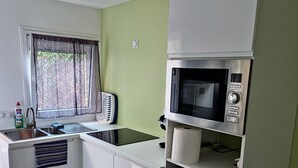 A modern kitchen with white cabinets, a built-in microwave, and a window with sheer curtains. - Studio Dépendance Quartier Tres Calme Proche de Paris (Les Pavillons-sous-Bois)