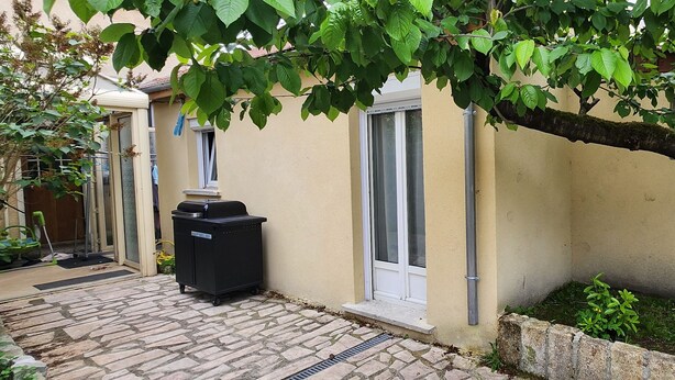 A residential building with a paved entrance, a trash bin, a tree, and a bicycle leaning against the wall. - Studio Dépendance Quartier Tres Calme Proche de Paris (Les Pavillons-sous-Bois)