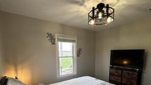 Een slaapkamer met een groot bed, een dressoir, een televisie en een raam met uitzicht op de omgeving.