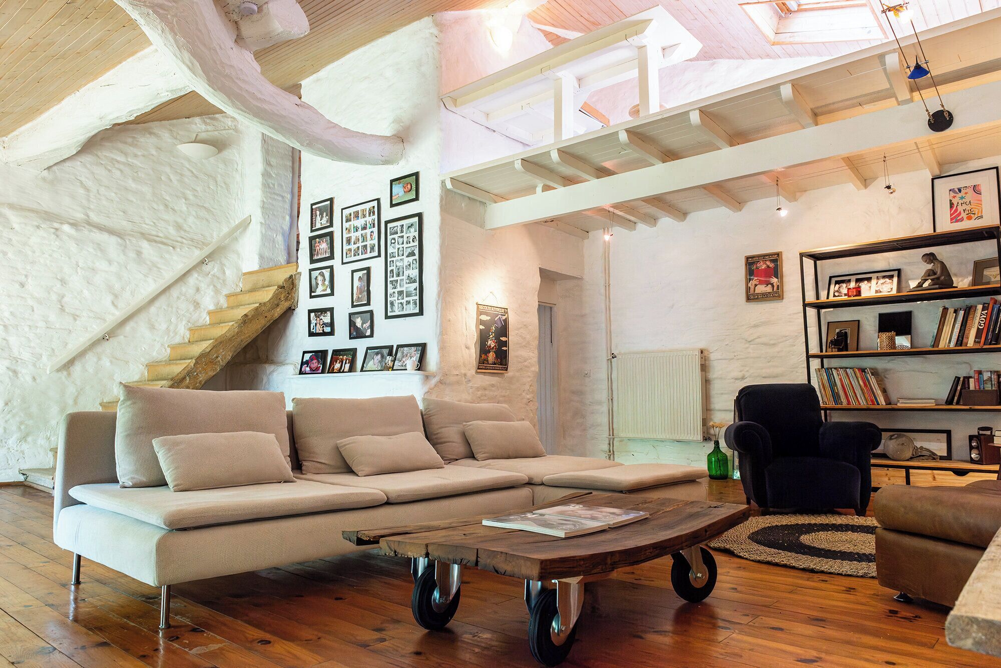 A cozy living room with a sofa, a coffee table, a bookshelf, and a staircase.