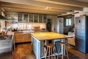 Una cocina con una isla central, taburetes de madera, electrodomésticos de acero inoxidable y un reloj en la pared.