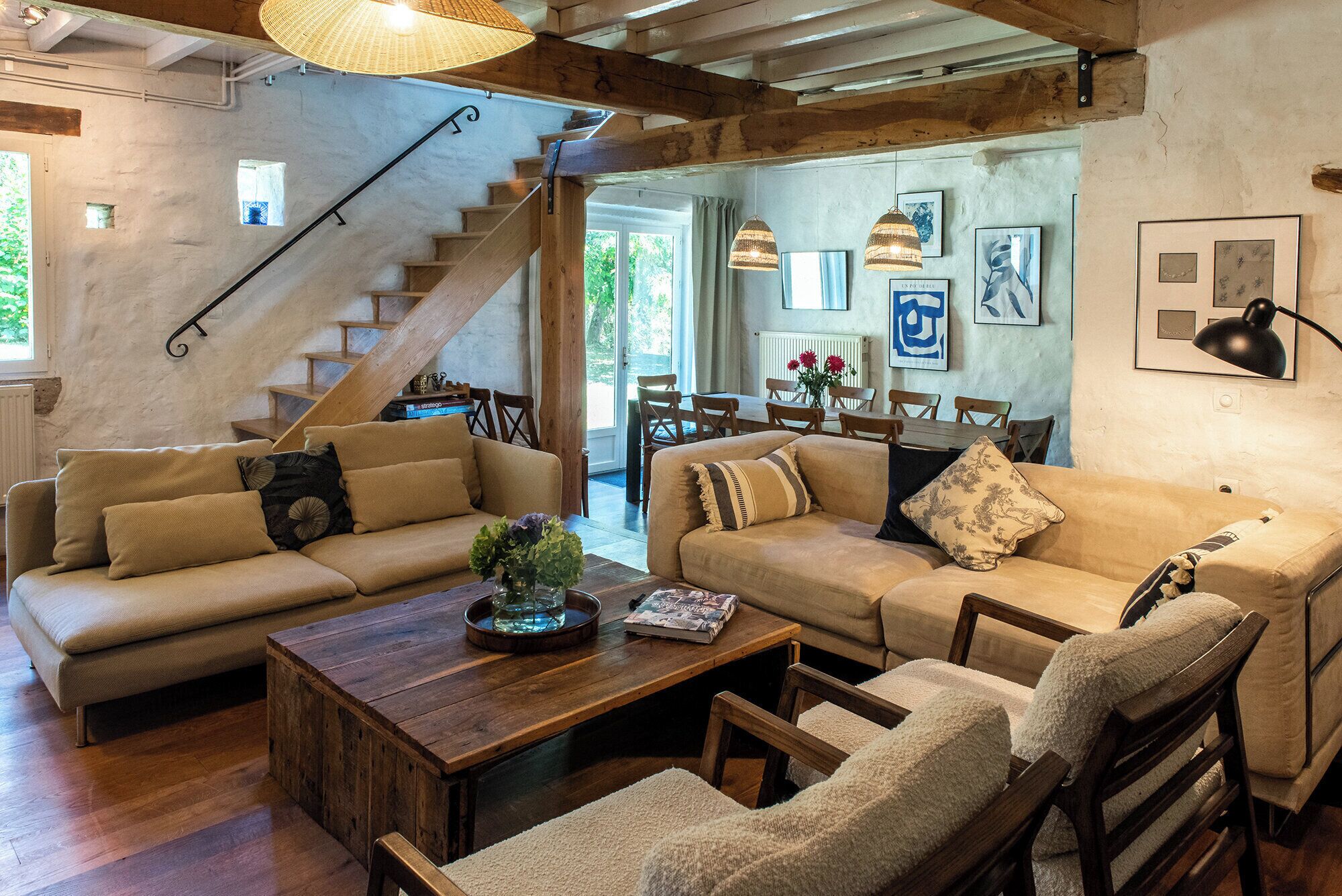 Een gezellige woonkamer met een houten trap, een eethoek en uitzicht op het landschap.