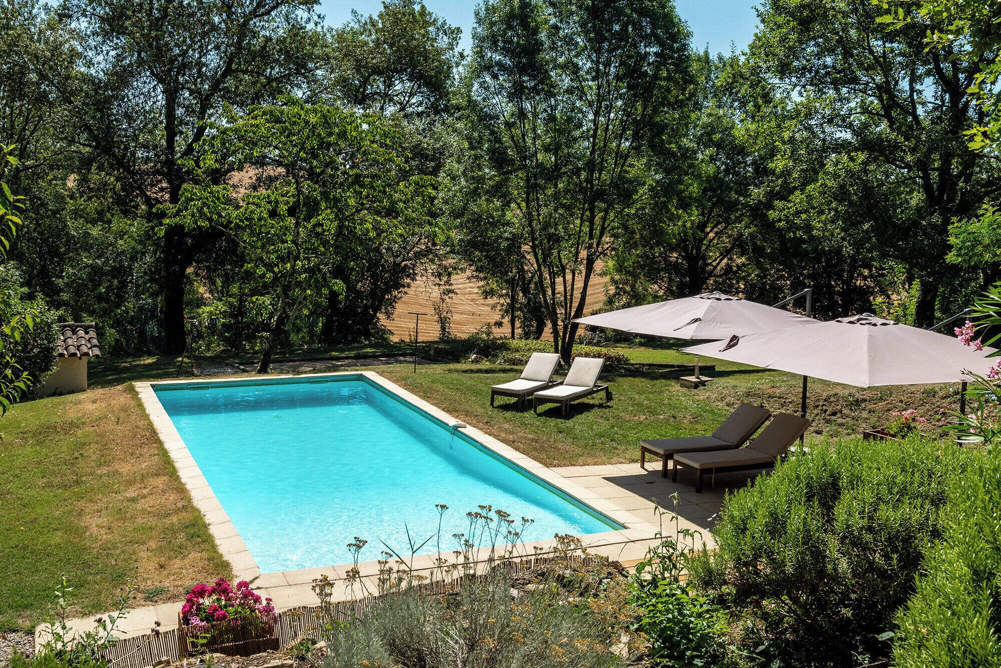 A rectangular swimming pool with a tiled edge, surrounded by a grassy area with two lounge chairs and a large umbrella.