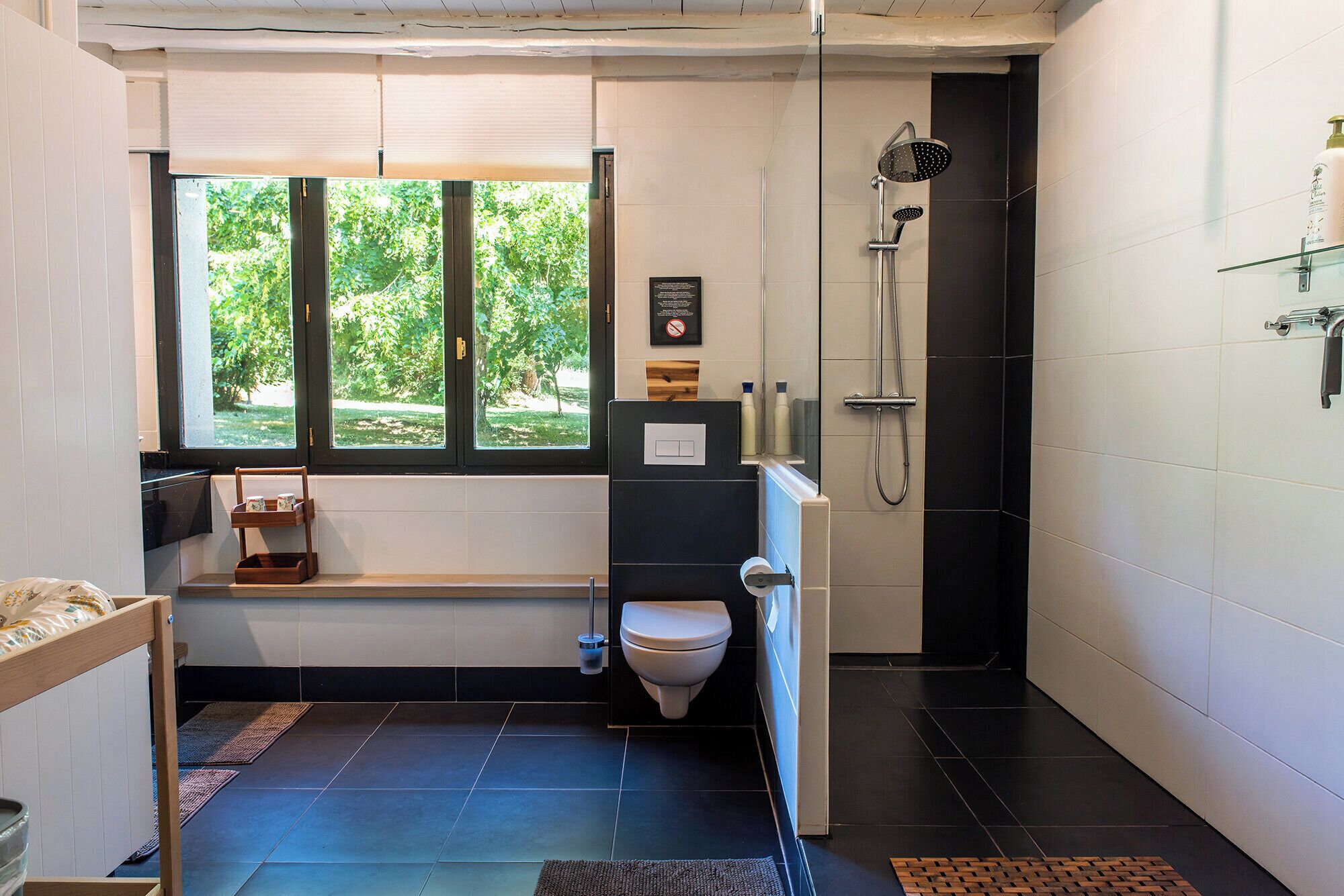 Et moderne badeværelse med bruser, toilet og et vindue med udsigt til grønne omgivelser.