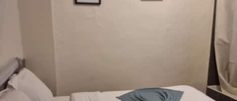 Une chambre d’hôtel avec un lit bien fait, un tableau encadré au mur et une étagère contenant des articles de toilette.
