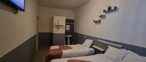 A hotel room with two beds, a television, a sink, and a mirror.