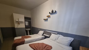 A hotel room with two beds, a small table, a wall-mounted shelf with decorative items, and a bathroom visible through an open door. - Hôtel Aboukir (Paris)
