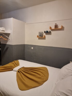 Une chambre d’hôtel avec deux lits, une petite étagère avec des articles de toilette et un porte-serviettes.