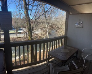 A covered outdoor area with a table and chairs, overlooking a body of water and trees.