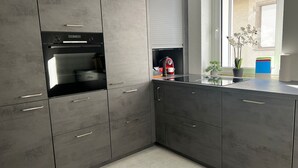 A modern kitchen with grey cabinets, a built-in oven, and a window with a view of the outside. - Ferienwohnung am Schönen Walensee in der Nähe der Gondelbahn Flumserberg (Unterterzen)