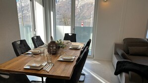 A dining area with a wooden table set for four, surrounded by black chairs. A plant is on the table, and a lamp is on the wall. - Ferienwohnung am Schönen Walensee in der Nähe der Gondelbahn Flumserberg (Unterterzen)