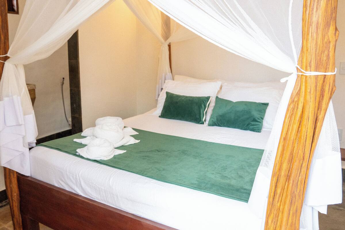 A neatly made bed with white linens, a green bedspread, and two green pillows.