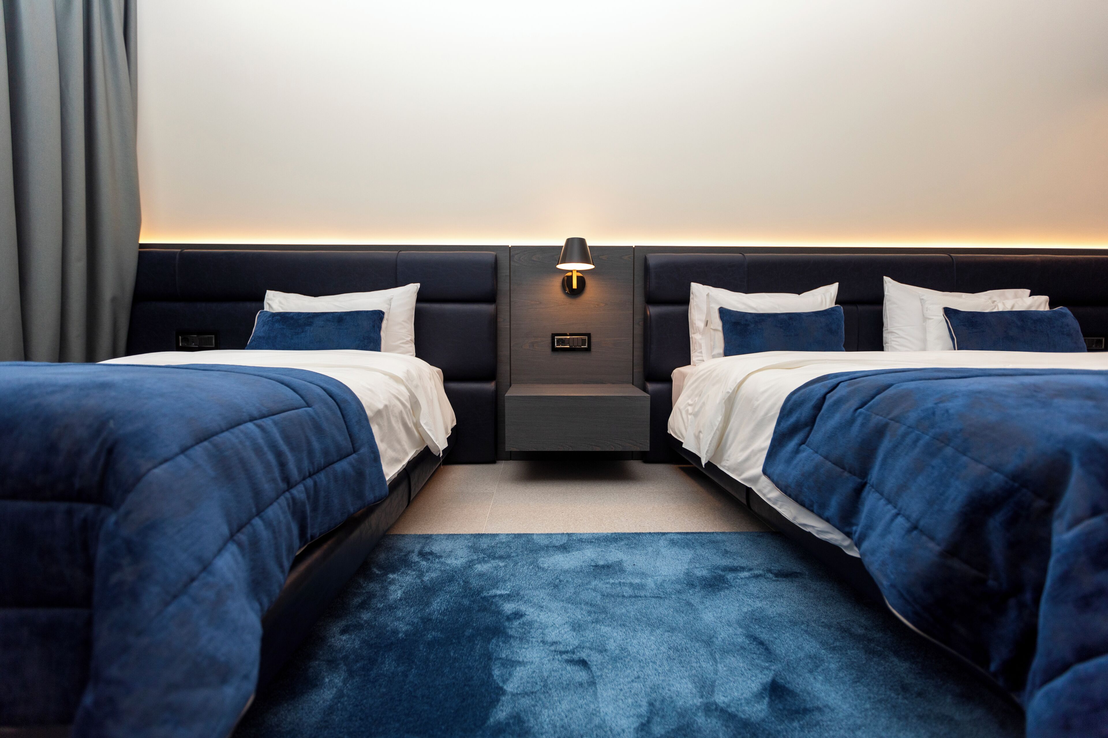 A hotel room with two beds, a nightstand, and a wall-mounted lamp.
