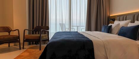 A hotel room with a large bed, a chair, a desk, and a view through the window.