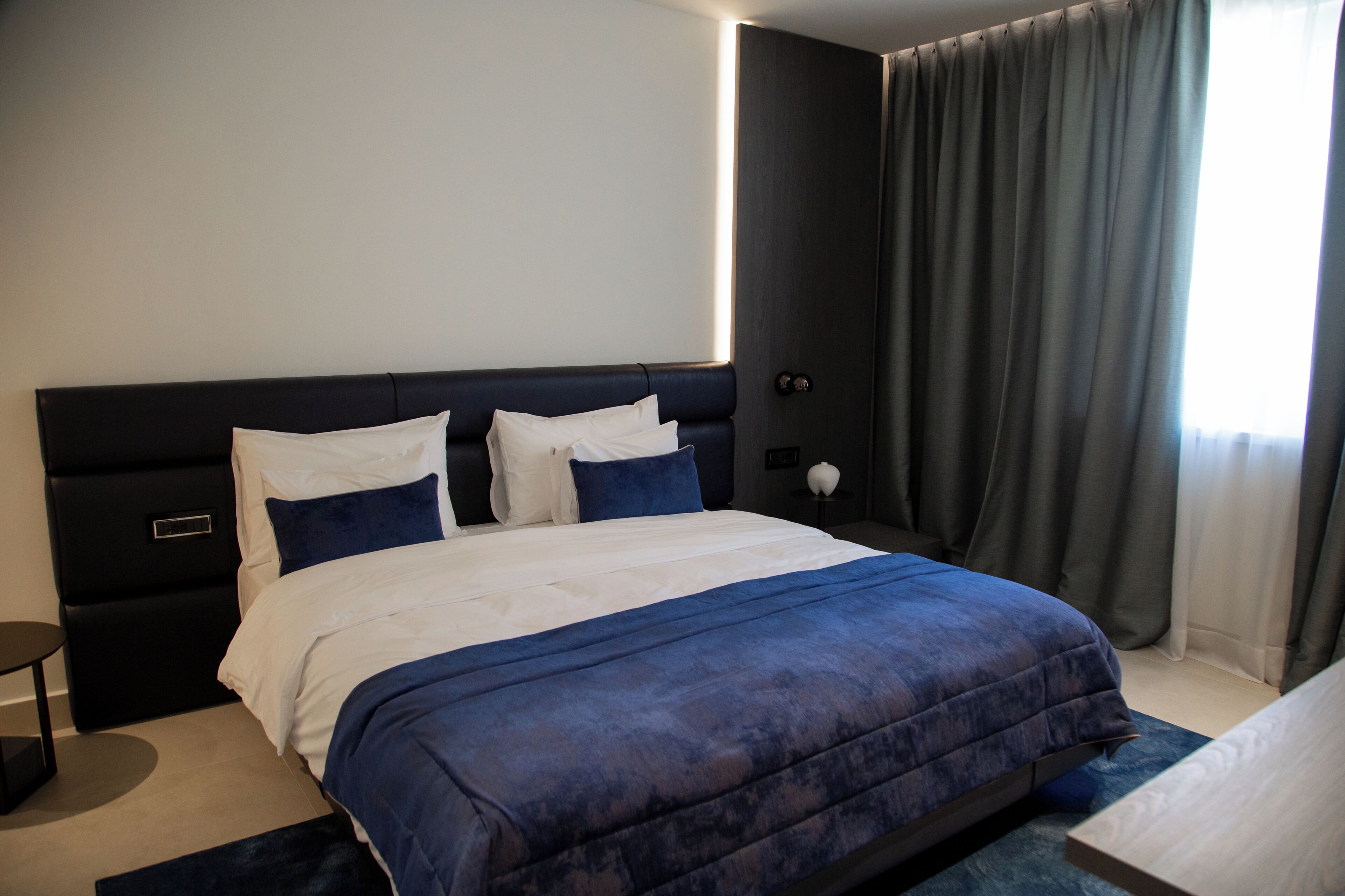 Habitación de hotel moderna con una cama grande, una mesita de noche y vistas al exterior.