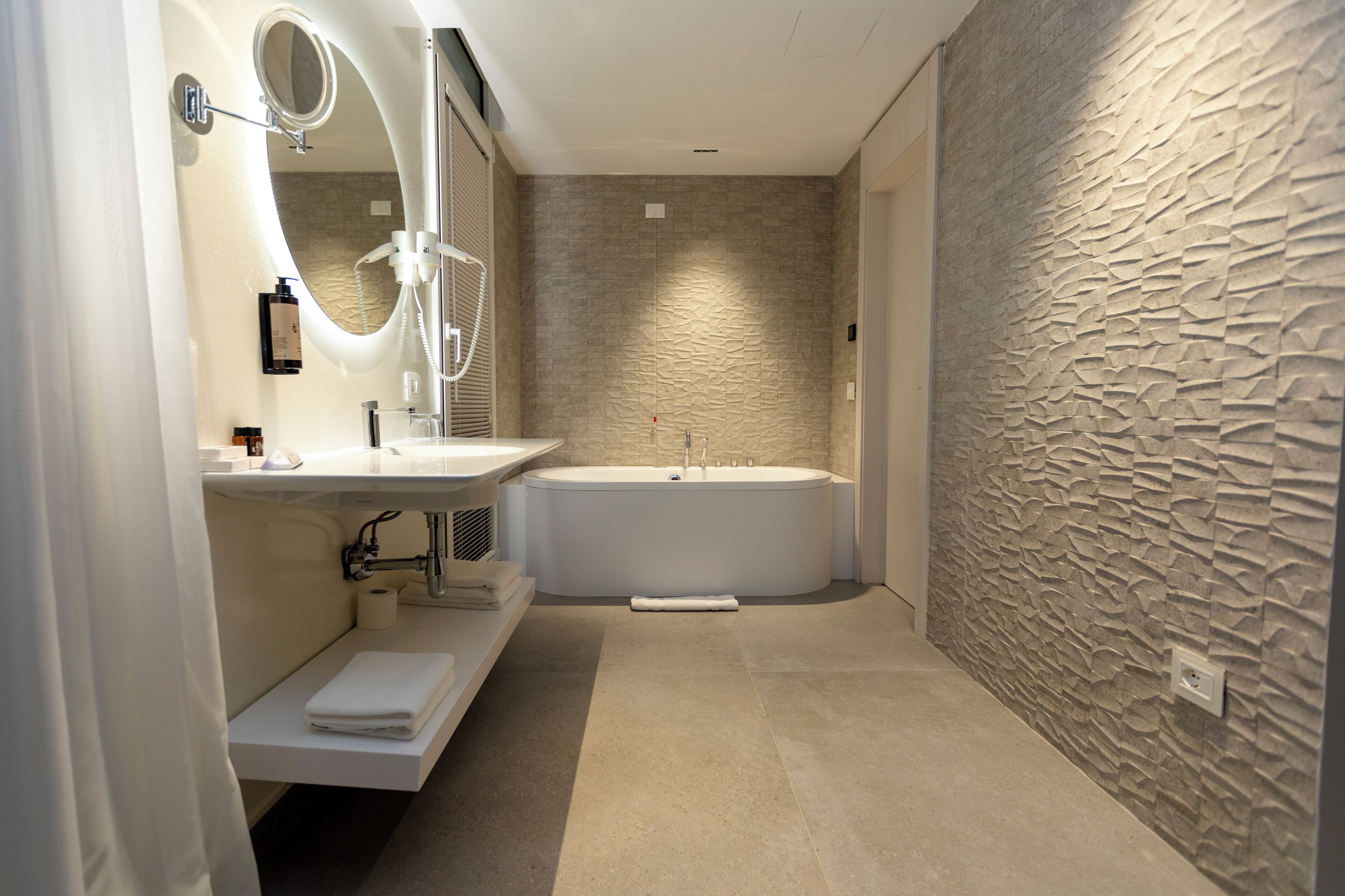 A modern bathroom with a freestanding bathtub, a vanity with a mirror, and a textured wall.