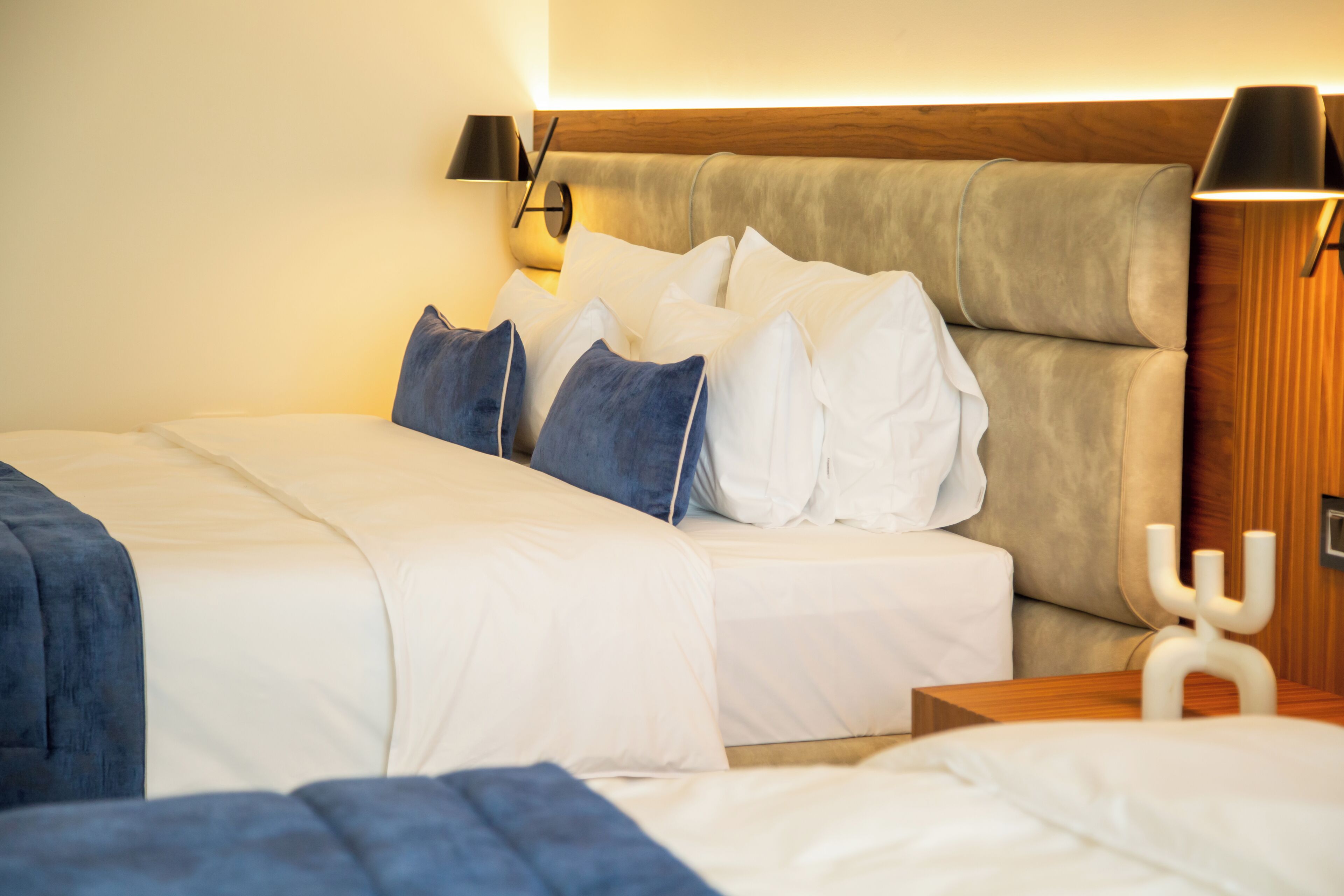 A hotel room with a bed, pillows, a bedside table, and a wall-mounted lamp.
