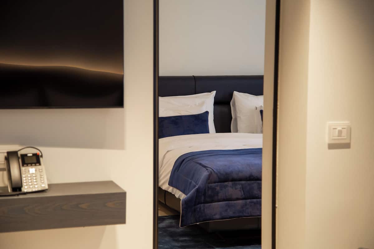 A hotel room with a bed, a bedside telephone, and a wall-mounted TV.