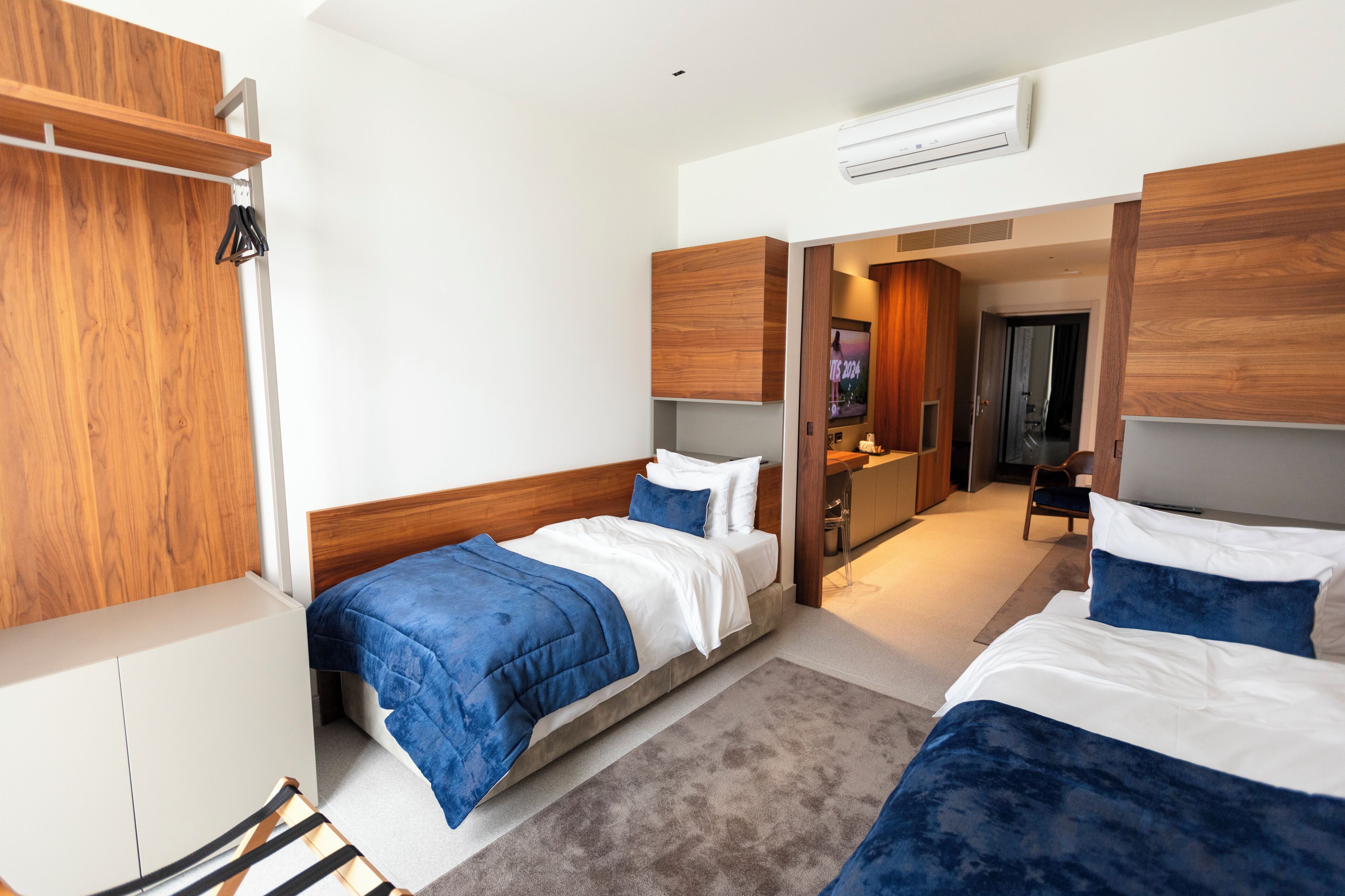 A hotel room with two beds, a wooden wardrobe, a shower area, and a television.