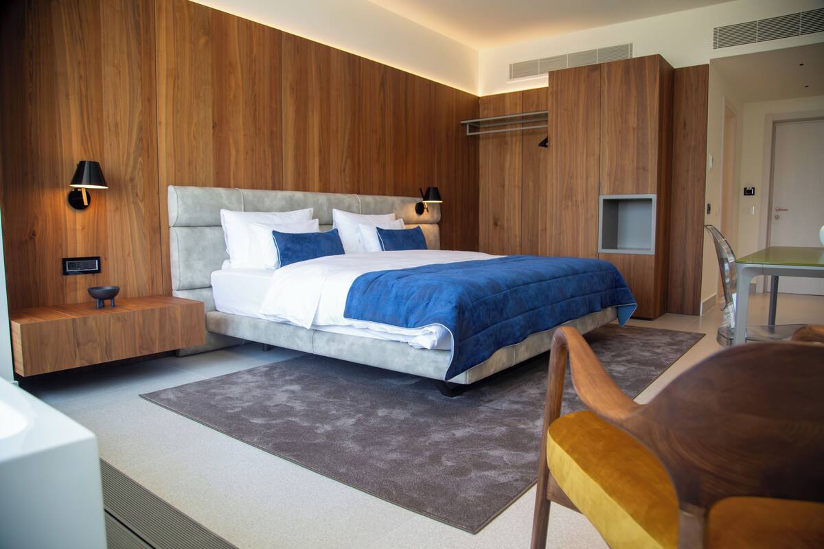 Ein modernes Schlafzimmer mit einem großen Bett, Holzwandverkleidung, einem Nachttisch mit Lampe und einem kleinen Regal.