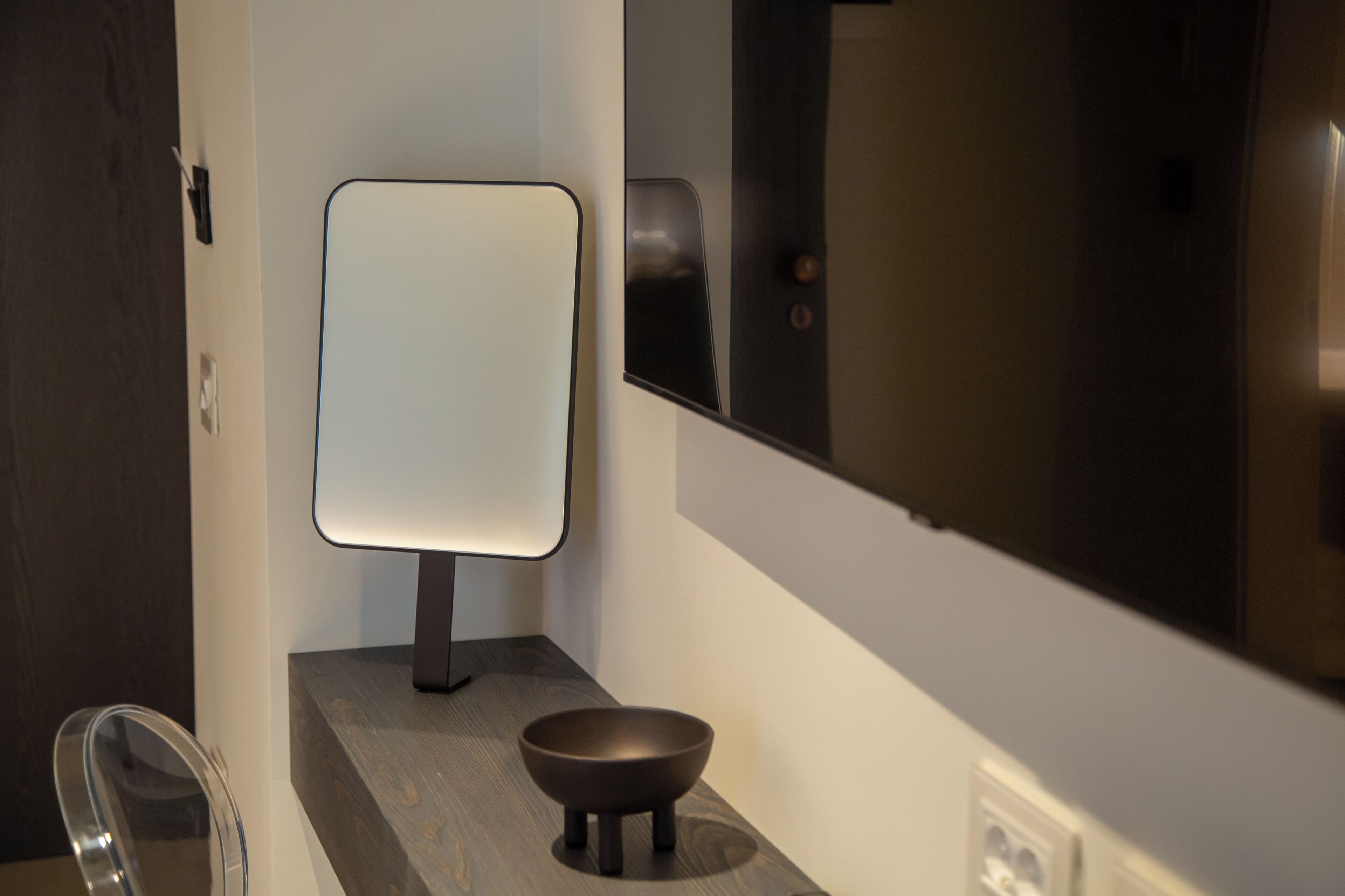 A modern bathroom with a minimalist design, featuring a dark wooden vanity, a white-framed mirror, and a small black bowl.