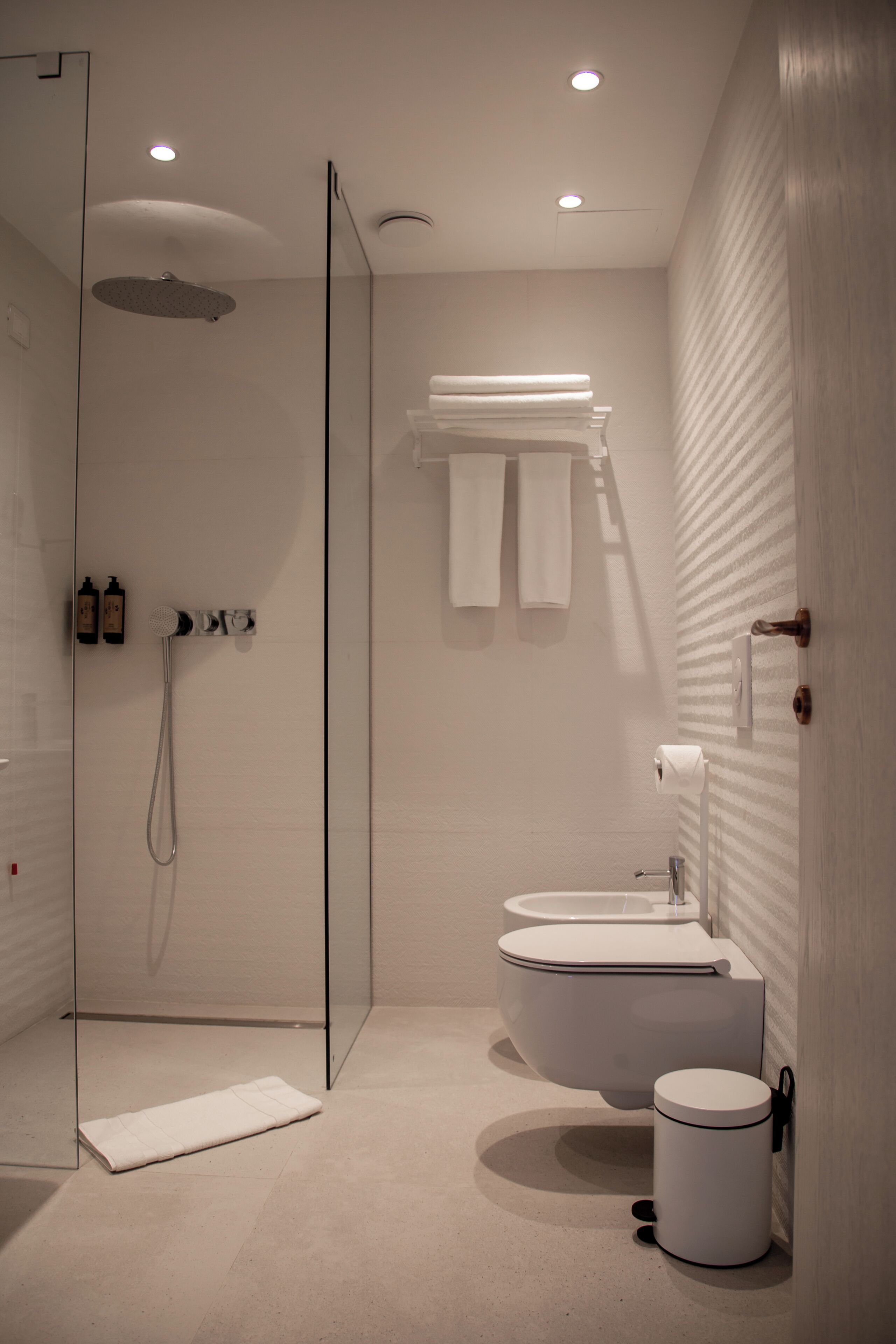 A modern bathroom with a glass shower enclosure, a freestanding bathtub, a toilet, and a towel rack.