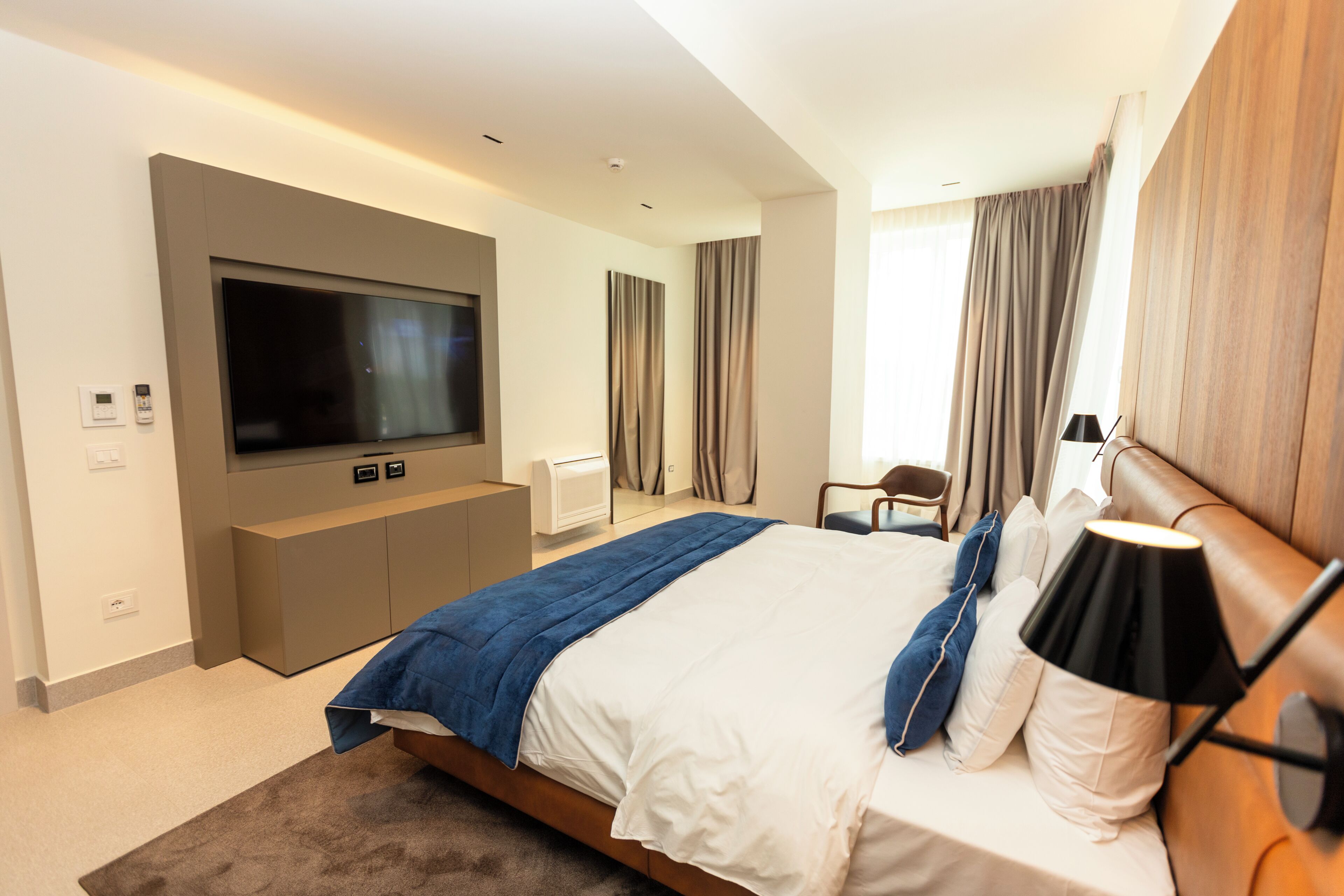 Una camera d'hotel moderna con un ampio letto, una TV a schermo piatto, una scrivania e una sedia.