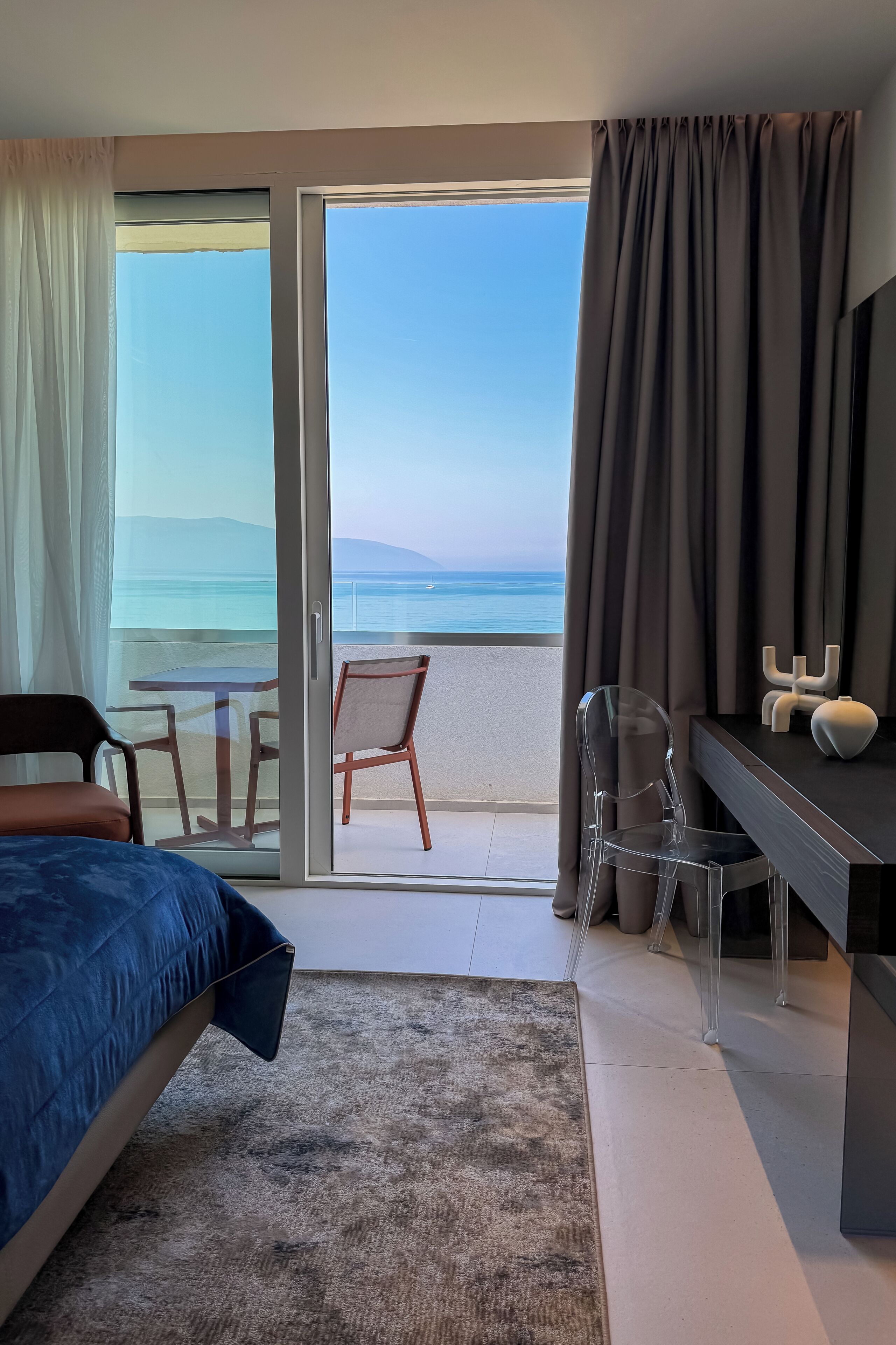 A hotel room with a bed, a desk, a chair, and a view of the sea.